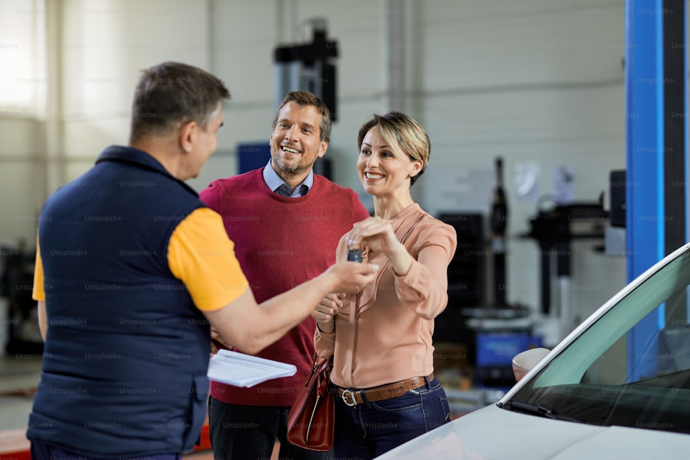 Happy couple handing over car keys to their auto repairman in a workshop.