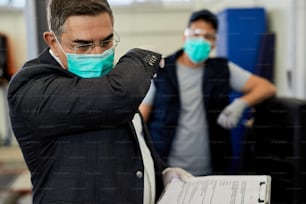 自動車整備工場で保護マスクを着用しながら肘に咳をする中年期の検査官。背景には作業員がいます。