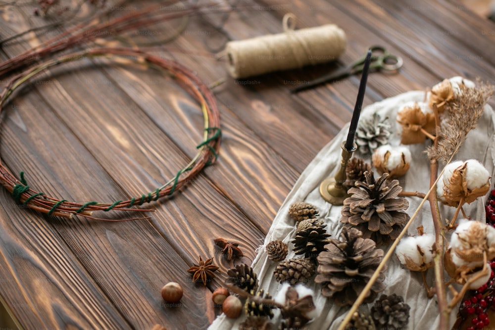 Décorations pour faire une couronne de Noël rustique. Pommes de pin décoratives, baies rouges, herbes, ficelle, coton et ciseaux sur fond en bois. Atelier de vacances
