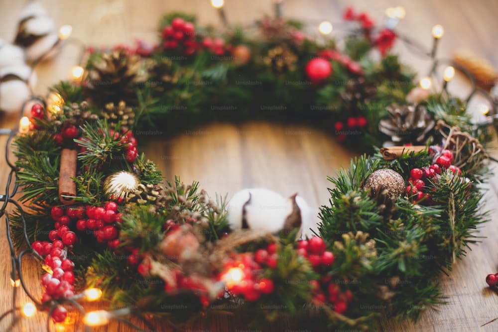 크리스마스 화환 장식은 조명의 소박한 나무에 닫힙니다. 목화, 붉은 열매, 장식품 및 소나무 콘 전통적인 크리스마스 화환, 휴일 워크샵. 텍스트를 위한 공간