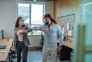 Informal greeting elbow bump by business people in the medical masks in the office during outbreak of the global pandemic COVID-19. Avoiding handshakes in a new normal. Selective focus on the man.