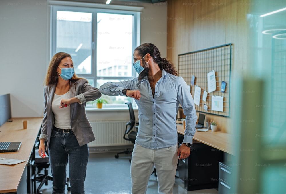 世界的なパンデミックCOVID-19の発生時にオフィスで医療用マスクを着用したビジネスマンによる非公式の挨拶肘のバンプ。ニューノーマルにおけるハンドシェイクの回避。男性に選択的に焦点を合わせます。