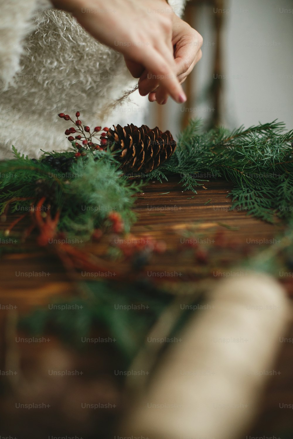 Making stylish rustic christmas wreath. Hands holding berries and decorating natural wreath on rustic wooden background. Seasonal holiday workshop or making wreath at home