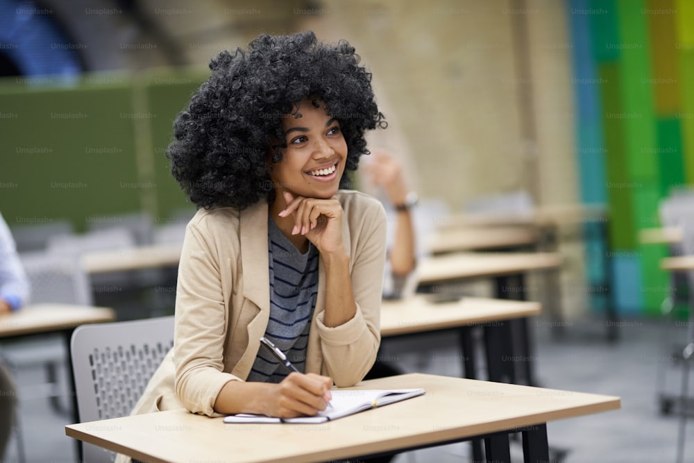 Happy mixed race businesswoman sitting at desk in the modern coworking space, listening to coach and smiling during corporate business training. Business people, leadership and self improvement