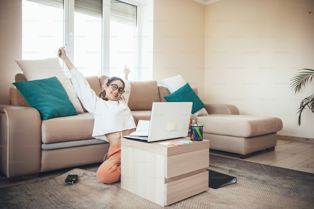 Caucasian girl with eyeglasses having online lessons on floor at the laptop gesturing the yes sign