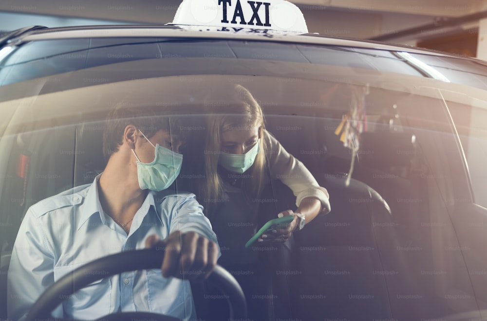 Nouvelle norme. Adolescent assis à l’arrière d’une voiture avec un masque. Jeune femme dans un taxi protégée par un masque. Sécurité routière. Pandémie de coronavirus. Utiliser un smartphone Trouver un itinéraire Voyage
