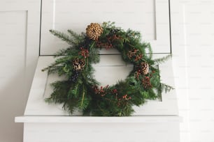 Rustic christmas wreath hanging on modern kitchen hood, festive holiday decoration. Creative modern christmas wreath hanging on stylish kitchen cabinets. Merry Christmas and Happy Holidays
