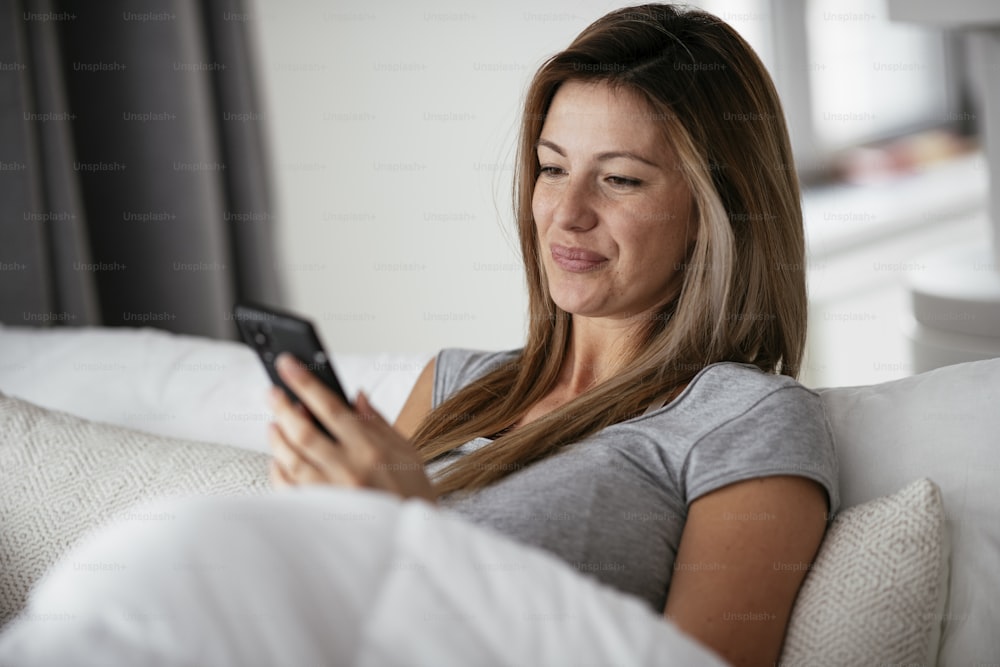 Young beautiful woman using phone in bed. Girl lying on bed.
