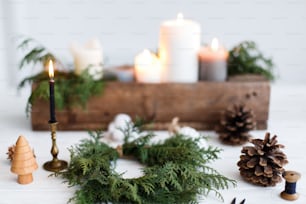 Fazendo simples coroa de Natal elegante com ramos de cedro, advento oficina de férias. Coroa de Natal rústica com velas, pinhas, fios e enfeites sobre mesa de madeira branca.