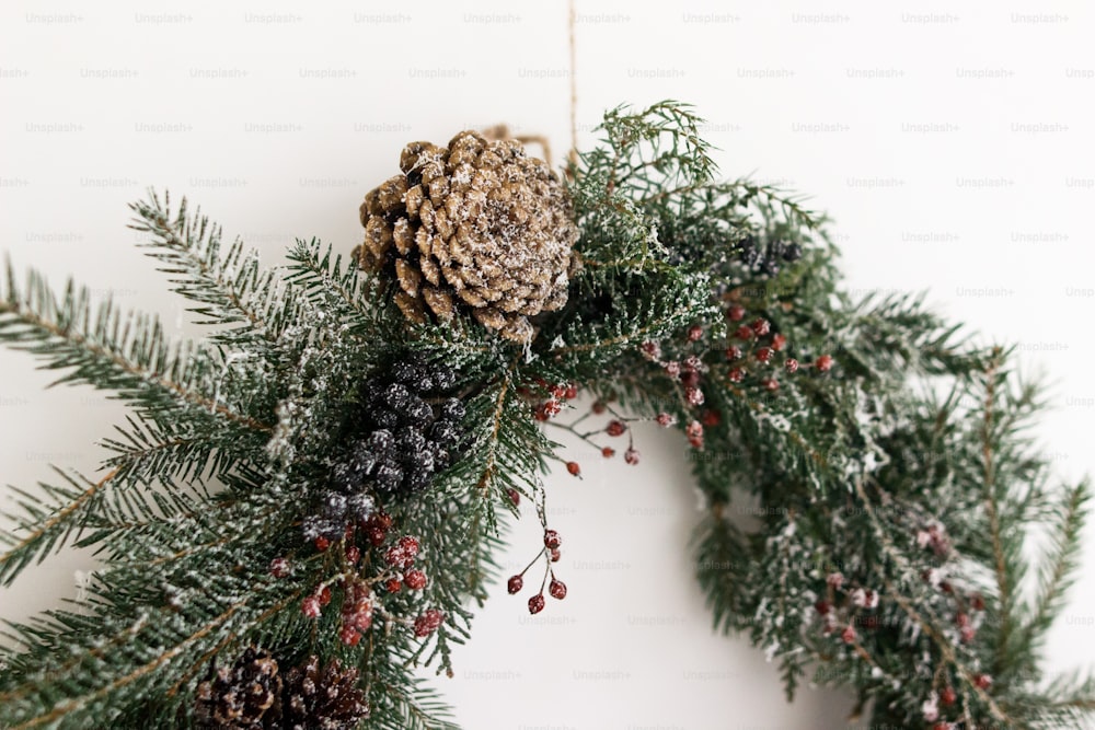 Creative stylish christmas wreath with pine cone and fir branches close up, isolated in white. Merry Christmas. Rustic christmas wreath hanging on white wall, festive modern decoration.