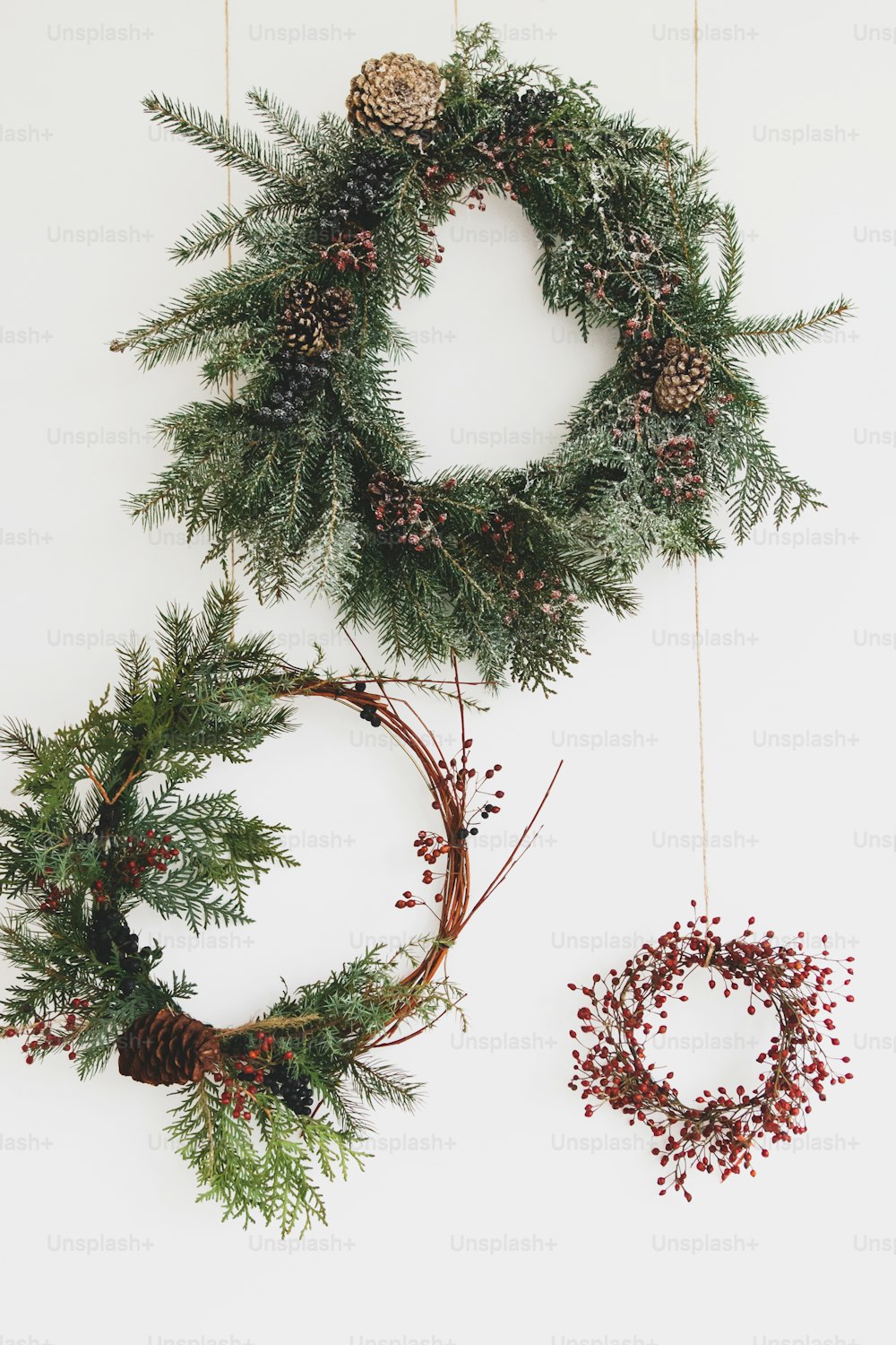 Rustic christmas wreath hanging on white wall, festive decoration. Creative natural and different christmas wreaths with red berries and fir branches, isolated on white. Merry Christmas