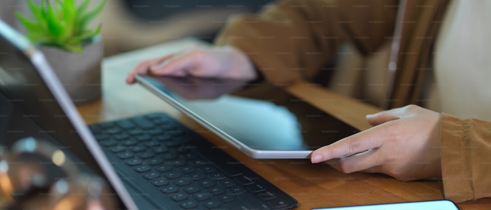 Abgeschnittene Aufnahme einer Frau, die ein digitales Tablet hält, während sie an einem Holztisch arbeitet