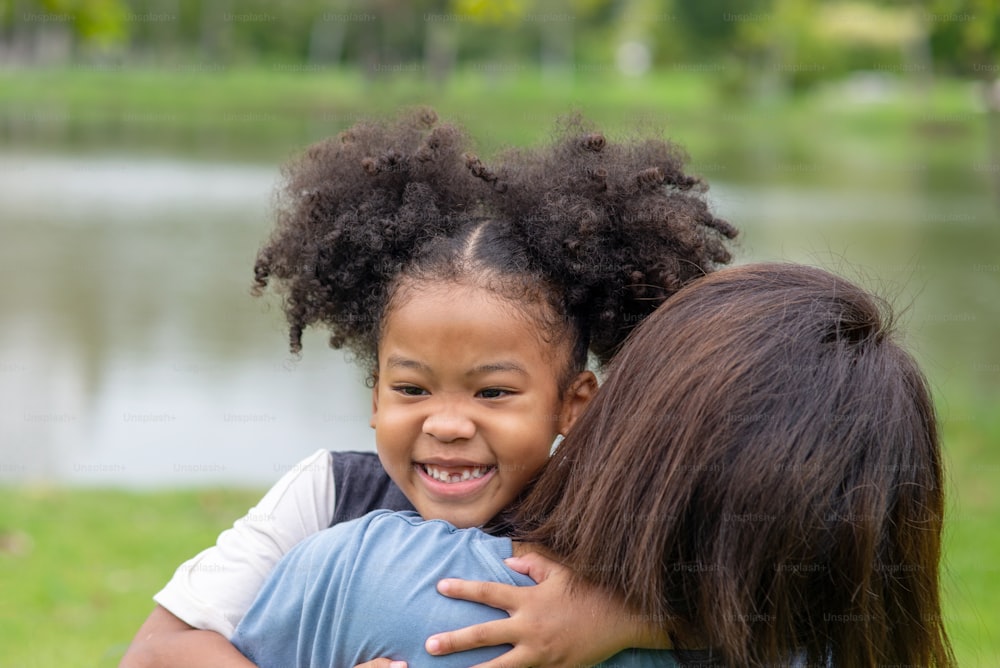 Fille métisse embrassant sa mère avec un sourire à pleines dents dans le parc