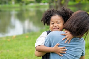 Mixed race daughter embracing her mother with toothy smile in the park