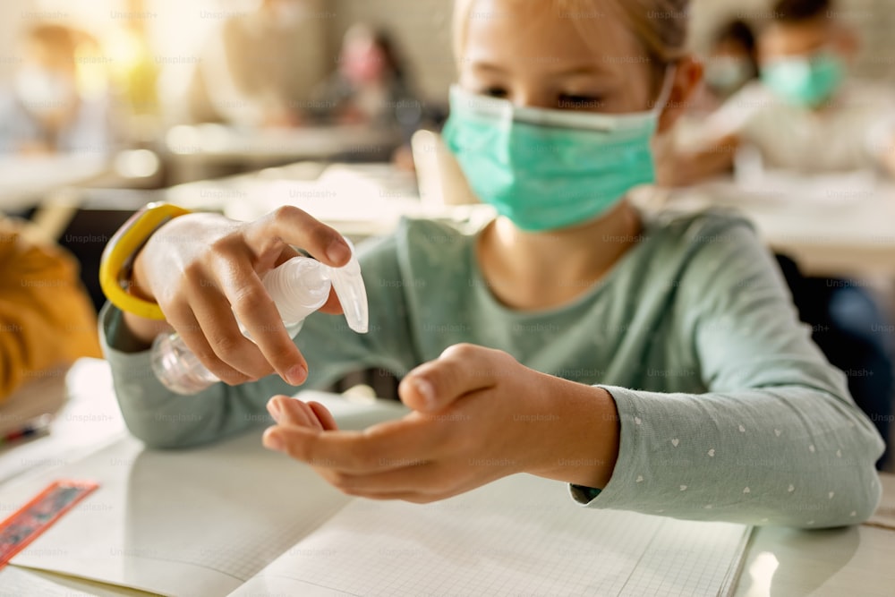 Close-up de aluno do ensino fundamental desinfetando as mãos na sala de aula devido à pandemia de COVID-19.