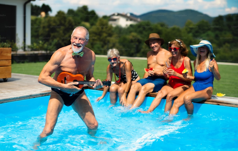 Gruppe fröhlicher Senioren mit Gitarre am Schwimmbad im Freien im Hinterhof, ein Partykonzept.