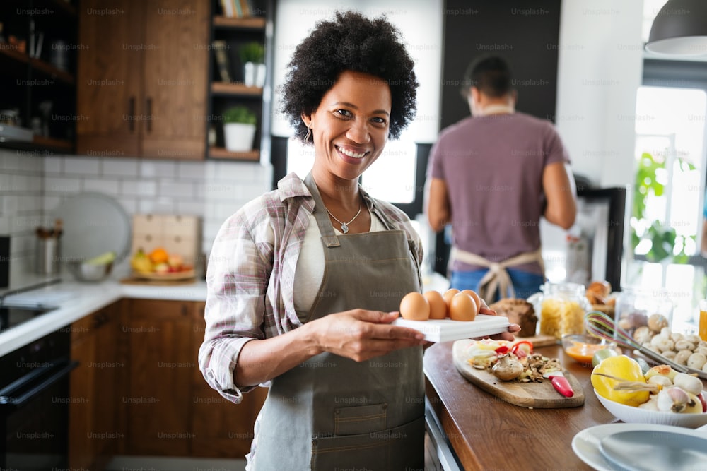 Happy african-american couple cooking and tasting healthy food in kitchen at home.