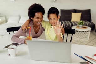 Happy black boy and his mother using computer while making video call at home.