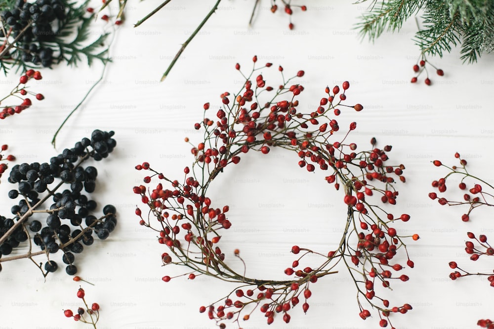 Simple Christmas wreath with red berries on rustic background. Making simple rustic christmas wreath on white wooden table at home, holiday advent