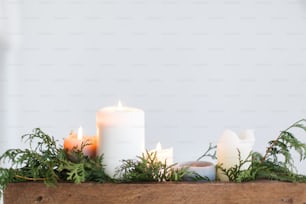 Burning candles in rustic wooden box with cedar branches on wooden table on white background. Festive christmas table decoration, winter holiday decor and wedding arrangement. Copy space
