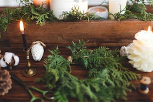 Realizzazione di una semplice ghirlanda di Natale elegante con rami di cedro, avvento del laboratorio di festa. Ghirlanda di Natale rustica con candele, pigne, filo e ornamenti su tavolo in legno.