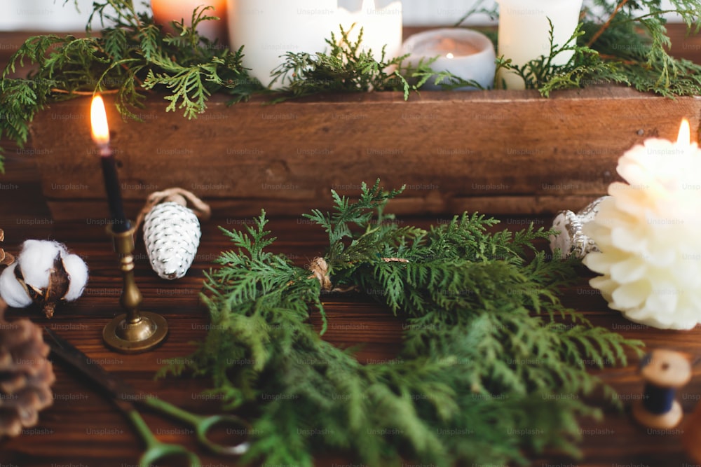 Making simple stylish christmas wreath with cedar branches, holiday workshop advent. Rustic christmas wreath with candles, pine cones, thread and ornaments on wooden table.