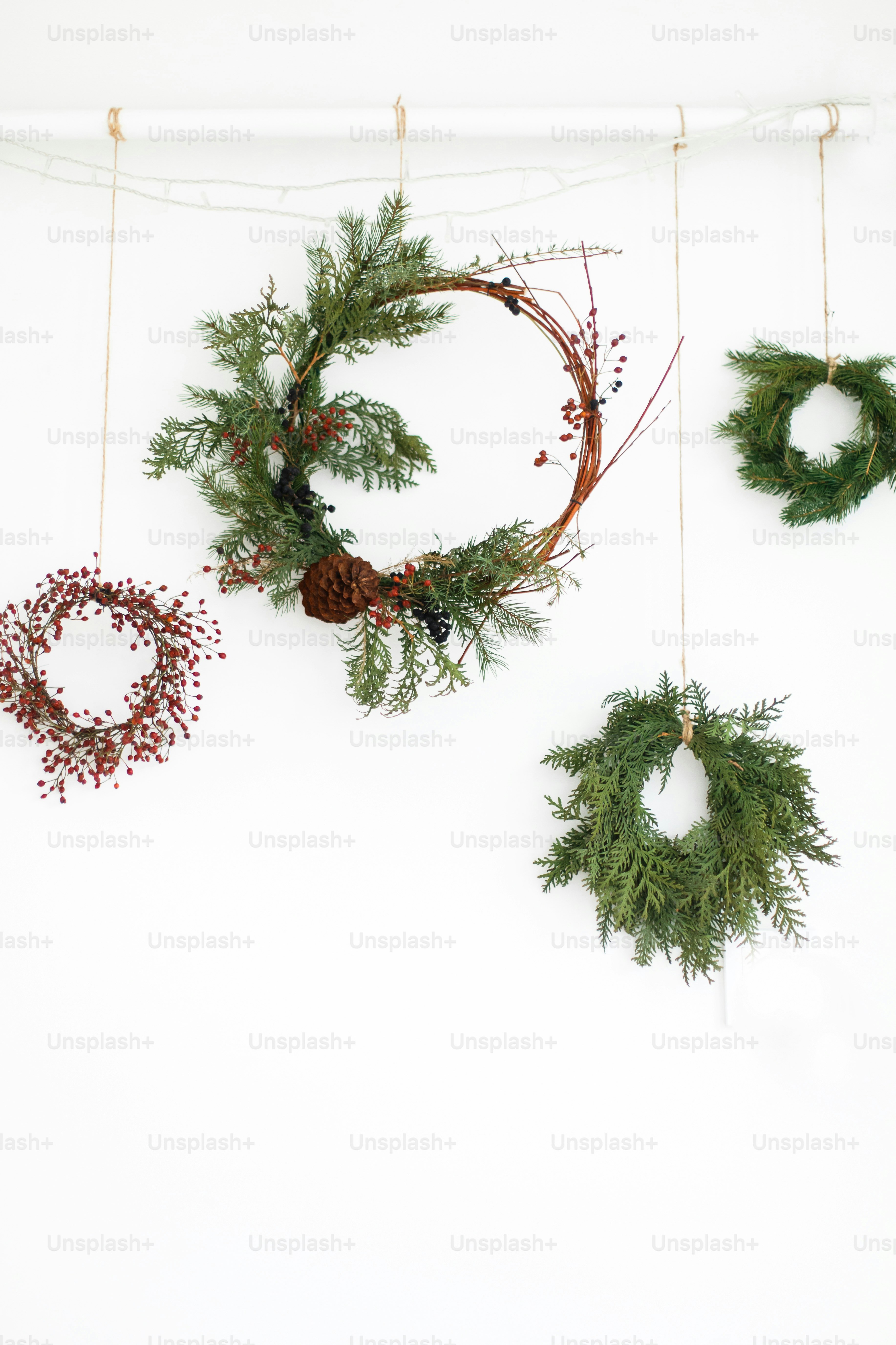 Creative natural and different christmas wreaths with red berries and fir branches, isolated on white. Merry Christmas. Rustic christmas wreath hanging on white wall, festive decoration