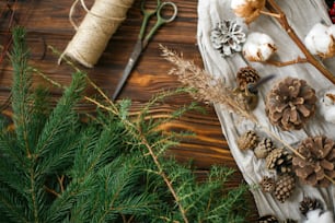 Christmas tree branches and decorations for making rustic christmas wreath at home. Natural fir branches, pine cones, herbs, twine, cotton and scissors on wooden background, top view