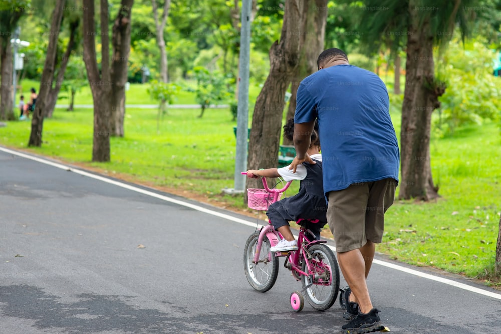 Happy African father teaching mixed race daughter to ride a bicycle in the park.