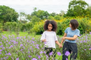 Happy mixed race mother with little daughter holding hands and walking together in the garden.
