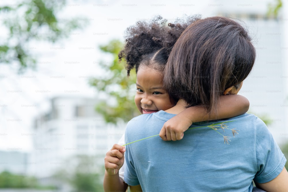 Gemischtrassige Tochter umarmt ihre Mutter mit zahnigem Lächeln im Park