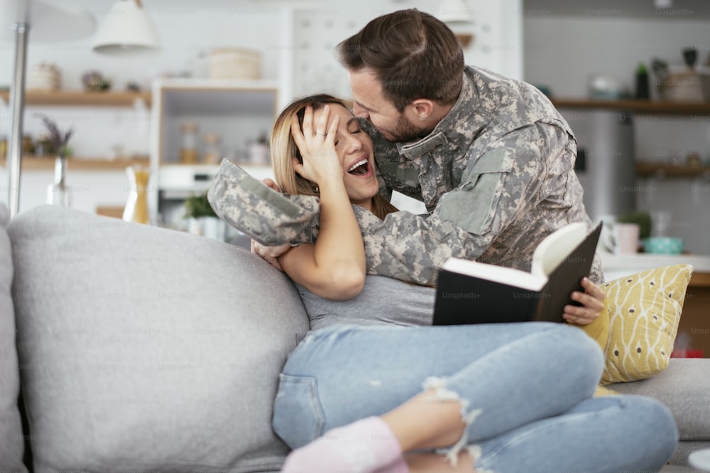 Happy soldier and his wife sitting on sofa at home. Young soldier hugging wife.