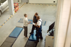 High angle view of auto mechanics communicating with a businesswoman in a workshop.