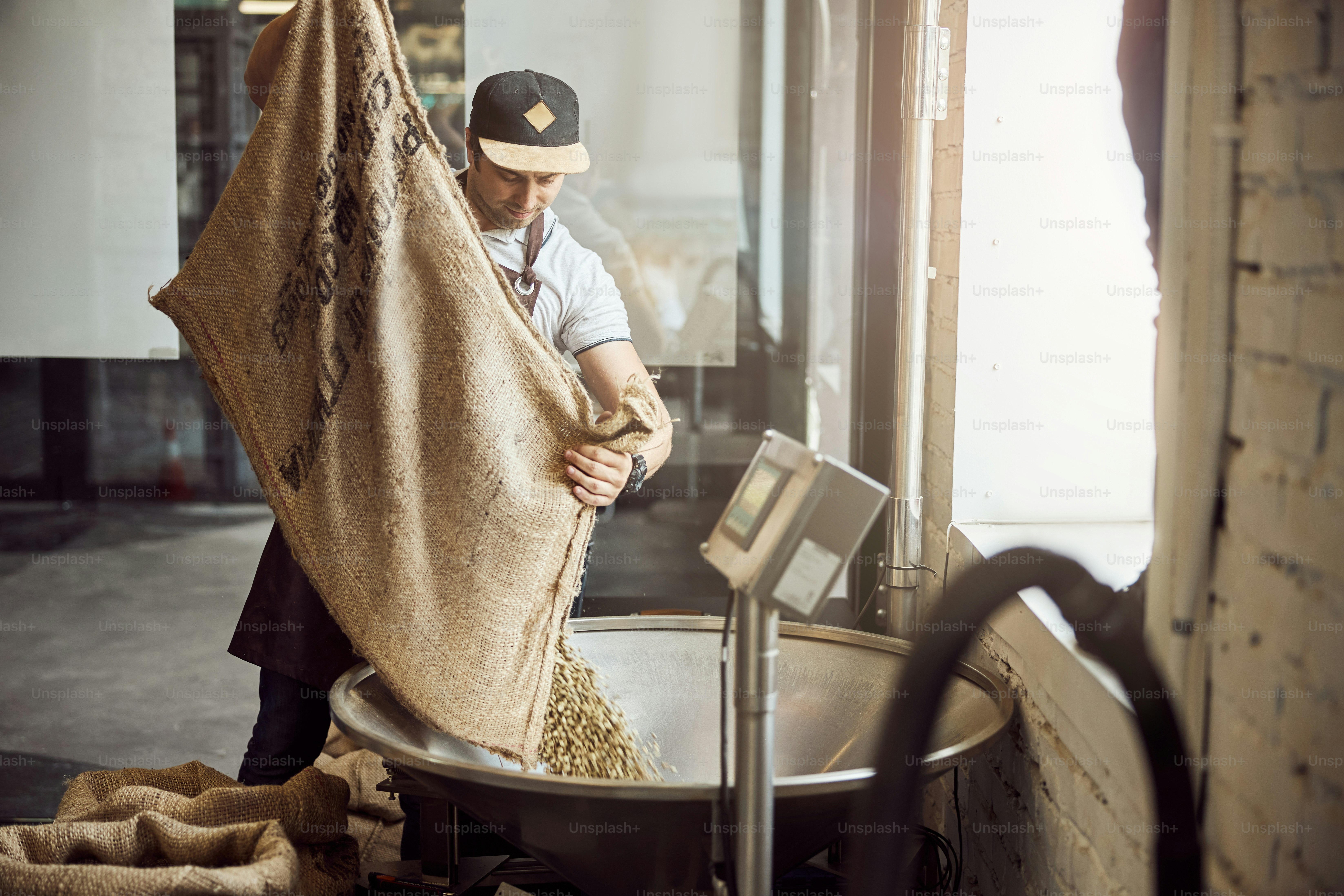 Gutaussehender junger Mann gießt ungeröstete Kaffeebohnen in Metalltrichter
