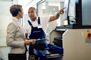 African American auto mechanic pointing at computer screen while talking to businesswoman in a workshop.