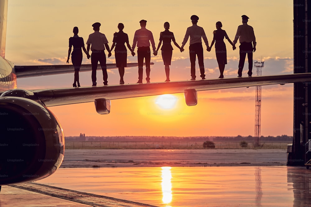 Portrait of pilots with women flight attendant in business uniform spending time in the aviation hangar while standing on the wing of commercial airplane