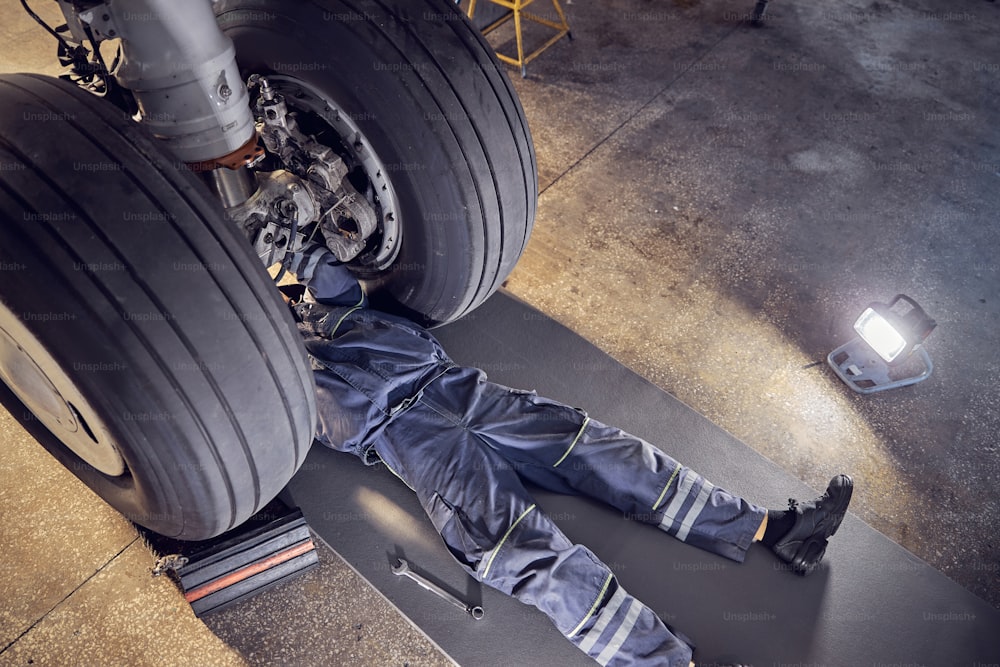 Top view portrait of aircraft engineer doing some maintenance on a landing gear of a big aircraft in a service hangar