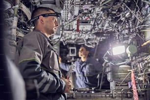 Side view portrait of two confident engineer working with electrical system of passenger aircraft
