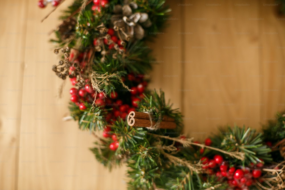 Corona de Navidad que cuelga en la puerta de madera rústica de la casa. Corona navideña tradicional con frutos rojos y adornos, piñas y canela sobre fondo de madera, decoración navideña.