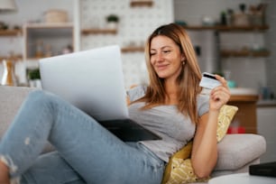 自宅の若い女性実業家がインターネットで買い物をする。クレジットカードを持つラップトップの美しい女性