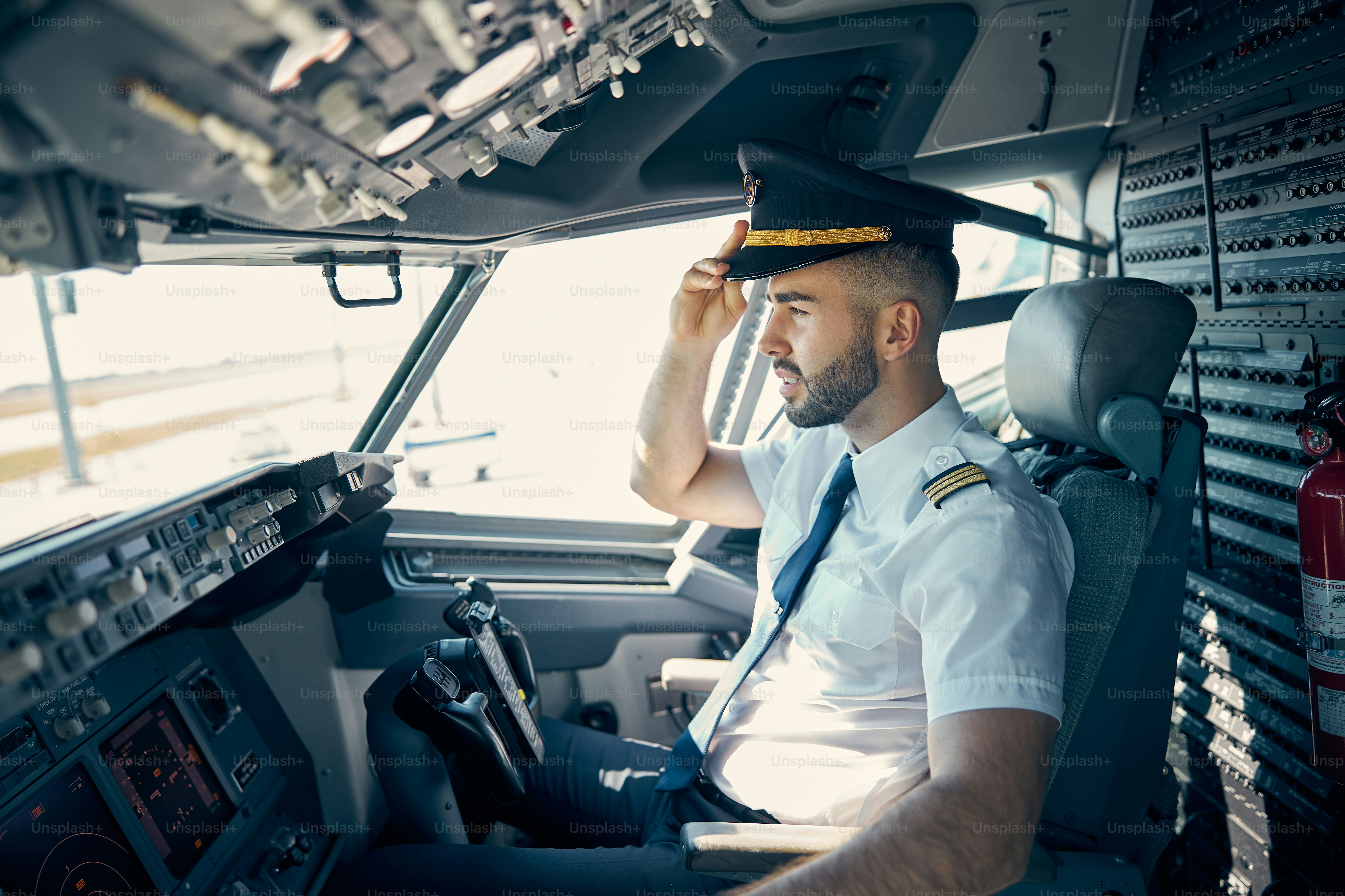Waist up side view portrait of confident male pilot in cap looking down from cockpit