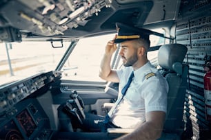 Retrato de la vista lateral de la cintura hacia arriba del piloto masculino confiado en la gorra mirando hacia abajo desde la cabina