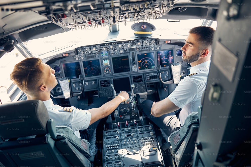 Vista posterior: retrato de dos pilotos discutiendo el plan de vuelo para su vuelo mientras están sentados en la silla en cabina