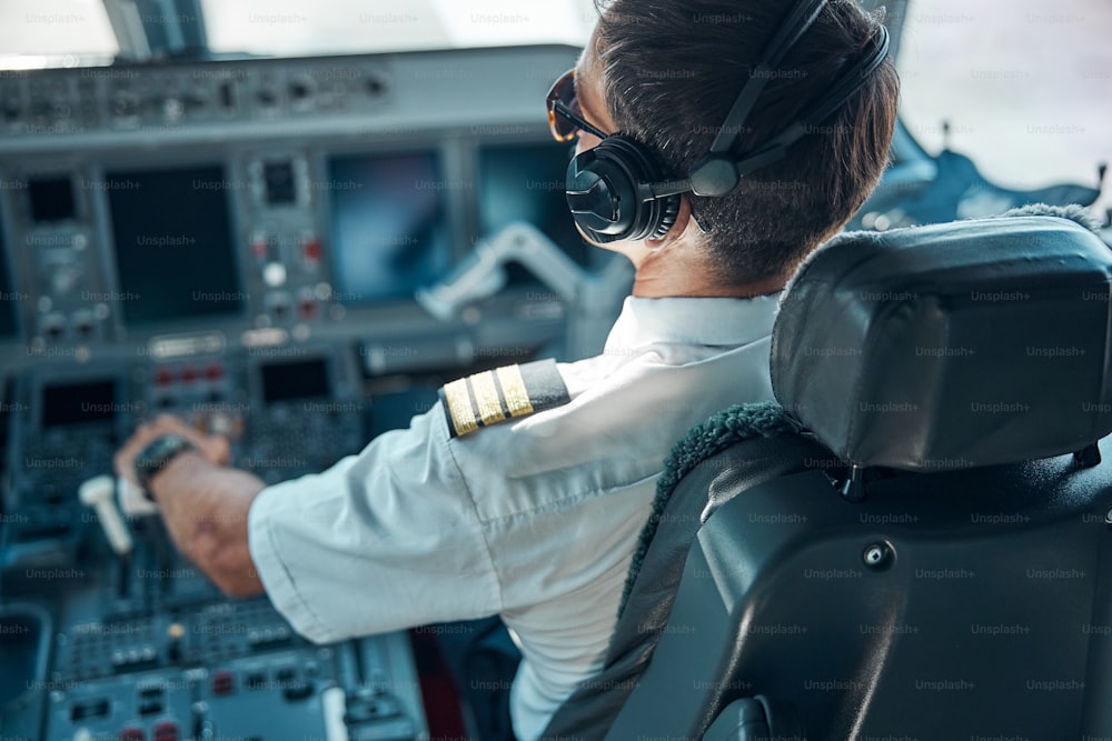 航空服とイヤホンを身に着けた男性が操縦席に座り、離陸中に舵を切っている様子を上から見た写真