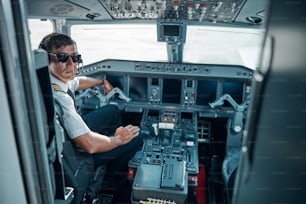 Cheerful young man in aircraft uniform and glasses near control is getting ready for flying jet