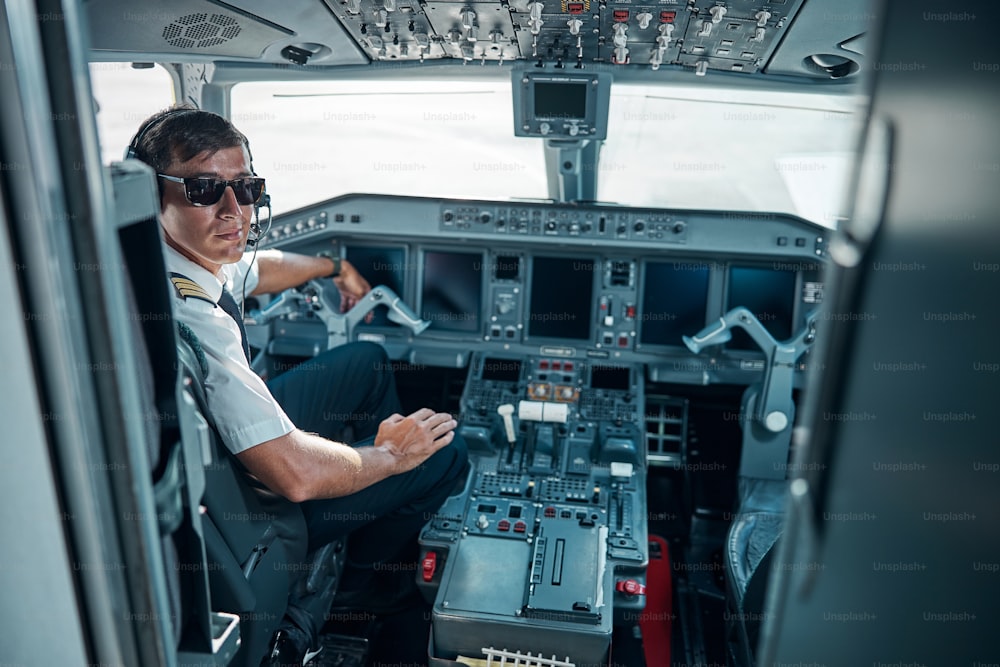 Cheerful young man in aircraft uniform and glasses near control is getting ready for flying jet