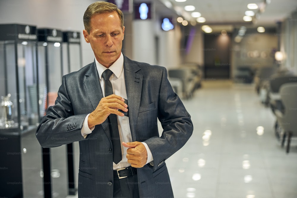 Elegant man in suit and tie is leaving lounge before departure and putting cel phone into pocket