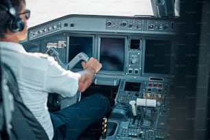 Un beau pilote portant des écouteurs et des lunettes est assis dans le cockpit et tient le gouvernail tout en décollant de la machine.