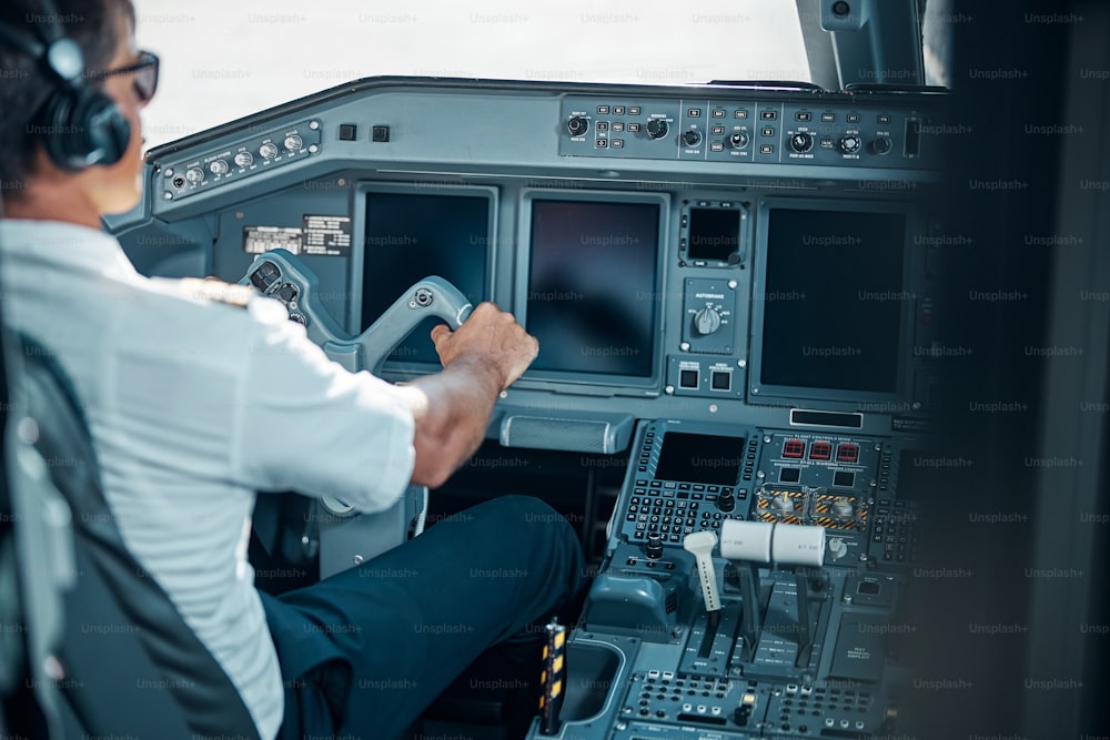 Handsome pilot in earphones and glasses is sitting in cockpit and holding rudder while taking off machine