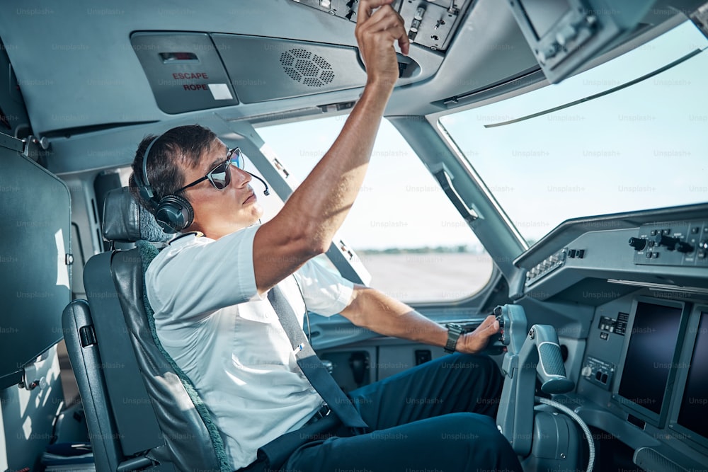 Ein gutaussehender Pilot mit Brille und Kopfhörern sitzt im Flugzeug und bereitet sich auf den Abflug vor